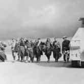Włoscy jeńcy wojenni, pod strażą strzelca karpackiego (pierwszy z prawej) w rejonie Autostrady Osi, Tobruk 1941. W tle samochód pancerny Marmon-Herrington w kamuflażu caunter. Źródło: Imperial War Museums